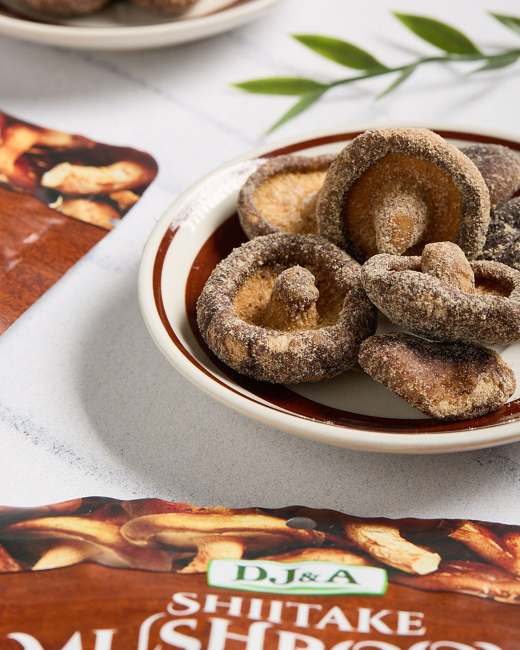 Dried shiitake mushrooms in a bowl next to a pack of DJ & A Shiitake Mushroom Crisps.
