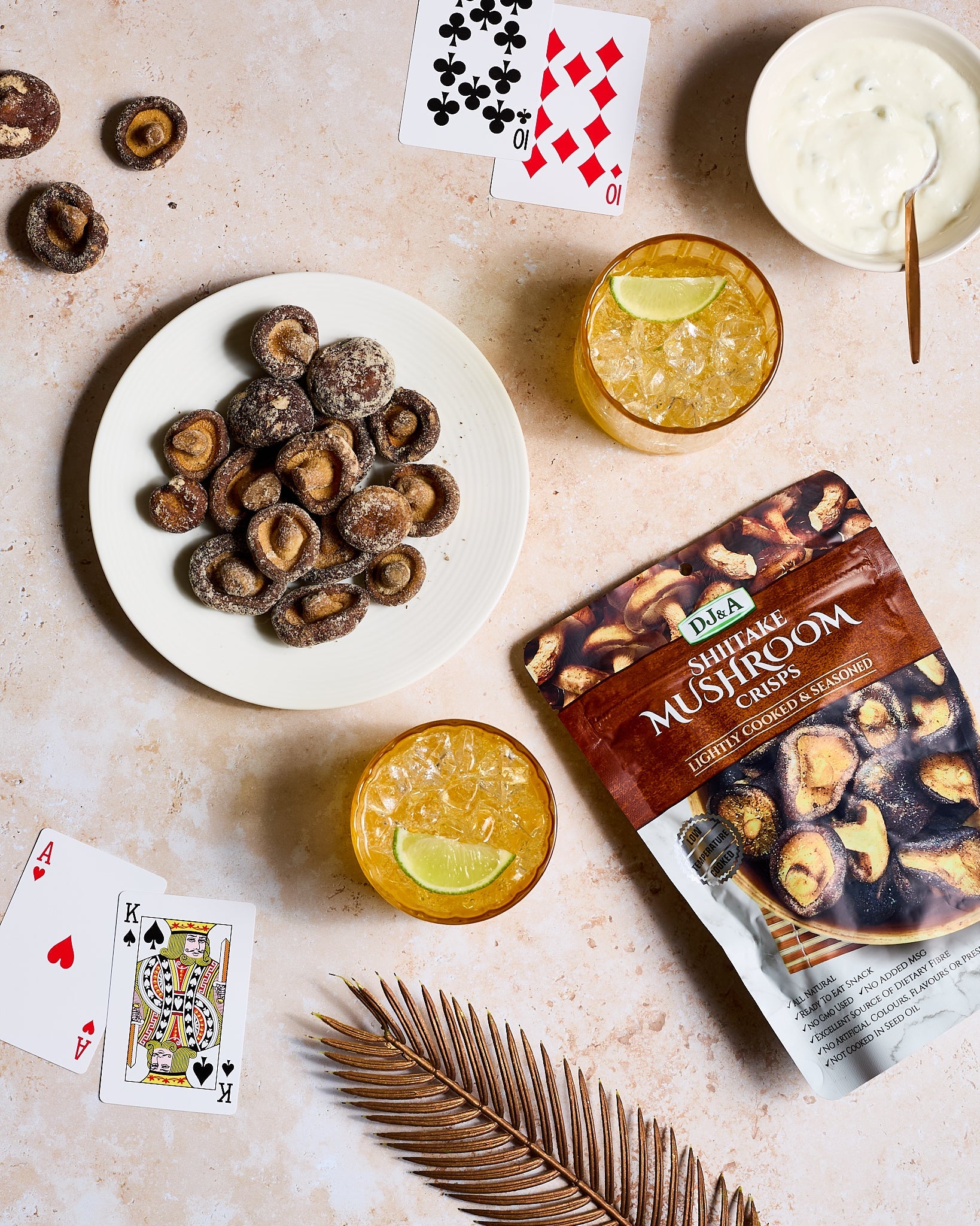 Shiitake mushroom crisps on a plate with cocktails and playing cards on a textured surface